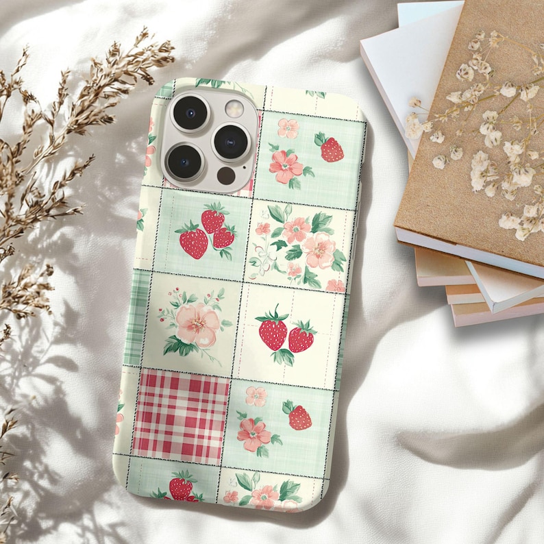 May include: A phone case with a patchwork design featuring strawberries and flowers on a white background. The case has a green and white checkered pattern in one of the squares.