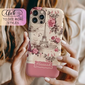 May include: A phone case featuring a vintage-style print of the Eiffel Tower, script text, and pink roses on a cream background. The lower section is a solid dusty pink color with a white label containing the name Hannah in cursive script.