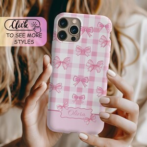 May include: A phone case featuring a light pink and white checkered pattern decorated with small pink bows. The lower section includes a rectangular label with the name Olivia printed in cursive script. A graphic overlay reads Click to see more styles.
