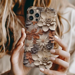 May include: A white and brown floral phone case with a raised 3D design. The case has a camera cutout for an iPhone.