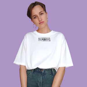 May include: A white t-shirt with the word "FEMINISM" printed in black on the front.