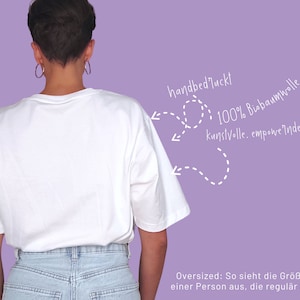May include: A white t-shirt with a relaxed fit, made from 100% organic cotton. The shirt is hand-sewn and features a unique design. The text "100% Biobaumwolle kunstvolle. empoweinde Designs" is written on the right side of the image.