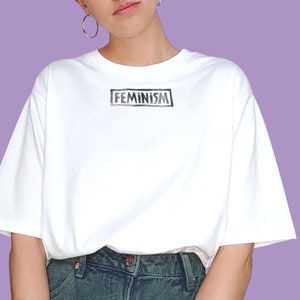 May include: White t-shirt with the word "FEMINISM" printed in a black box on the front.