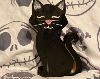 May include: Black wooden cat figurine with white whiskers and a pink nose. The cat is sitting with its tail curled around its body.