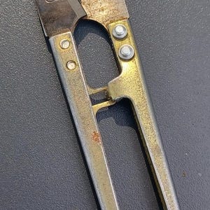 May include: Close-up of a pair of vintage silver and gold thread snips. The blades are slightly open, showing signs of wear and rust. The handles have a loop design for easy grip, and are riveted together.