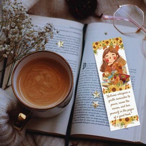 Puede incluir: Un marcapáginas con una ilustración de acuarela de una persona leyendo un libro con una taza de café. El marcapáginas tiene una cita que dice: "El otoño susurra un suave recordatorio para hacer una pausa, saborear la estación y perderse en las páginas de un buen libro."