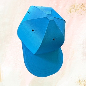 Puede incluir: Una gorra de béisbol azul brillante con un diseño geométrico único. La gorra tiene una visera curvada y una corona estructurada con cuatro agujeros espaciados uniformemente.