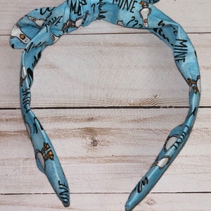 May include: A blue headband with a white and black pattern of ducks and the text "Mine" repeated throughout.