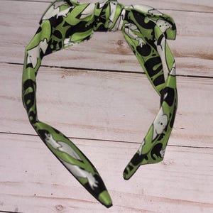 May include: A green headband with a white ghost pattern. The headband is tied in a bow at the top.
