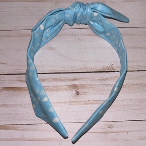 May include: A light blue headband with a white polka dot pattern. The headband is tied in a knot at the top.