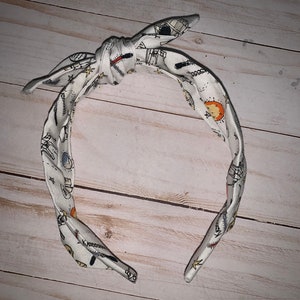 May include: A white headband with a black and white print of stars, planets, and spaceships. The headband is tied in a knot at the top.