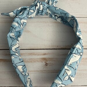May include: A light blue headband with a white shark pattern. The headband is tied in a knot at the top.