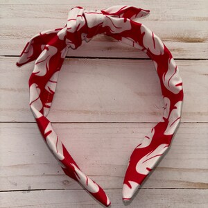 May include: A red and white headband with a floral pattern. The headband is tied in a knot at the top.