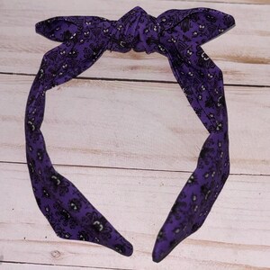 May include: Purple headband with a black and white ghost pattern. The headband is tied in a knot at the top.