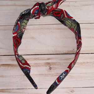 May include: A red, white, and blue patterned headband with a knot on top. The headband is made of fabric and has a black elastic band.