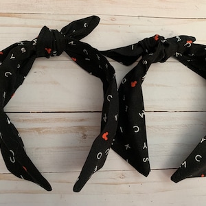 May include: Two black headbands with a white alphabet and red Mickey Mouse print. The headbands are tied in a knot at the top.