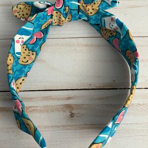 May include: A blue headband with a white and pink pattern of cookies and milk cartons. The headband is tied in a knot at the top.
