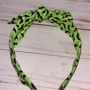 May include: A green headband with a black bat pattern. The headband is tied in a bow at the top.