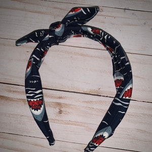 May include: A blue headband with a white and red shark print. The shark has the words "Always Hungry" written on it.