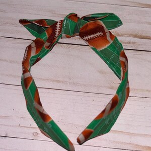 May include: Green and brown headband with a football field and football pattern. The headband is tied in a bow at the top.