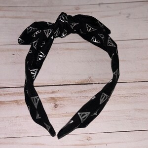 May include: Black headband with a silver print of the Deathly Hallows symbol repeated all over the fabric.