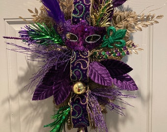 May include: Purple, gold, and green Mardi Gras door wreath with a masquerade mask, feathers, and a green and gold ornament.