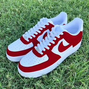 Pu&ograve; includere: Un paio di scarpe da ginnastica bianche e rosse con un logo Swoosh rosso. Le scarpe hanno una suola bianca e una tomaia rossa.