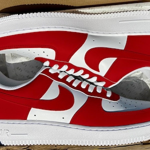 Pu&ograve; includere: Un paio di scarpe da ginnastica bianche e rosse con un logo Nike bianco. Le scarpe sono in una scatola di scarpe.