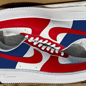 May include: A pair of low-top sneakers in a white, red, and navy blue color scheme. The shoes feature a white base with red overlays on the toe and mid-panel, a navy blue heel panel, and a red swoosh logo on the side. The white midsole has the text AIR.