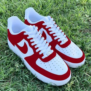 Pu&ograve; includere: Un paio di scarpe da ginnastica bianche e rosse con un logo swoosh bianco. Le scarpe hanno una punta e un tallone in camoscio rosso.