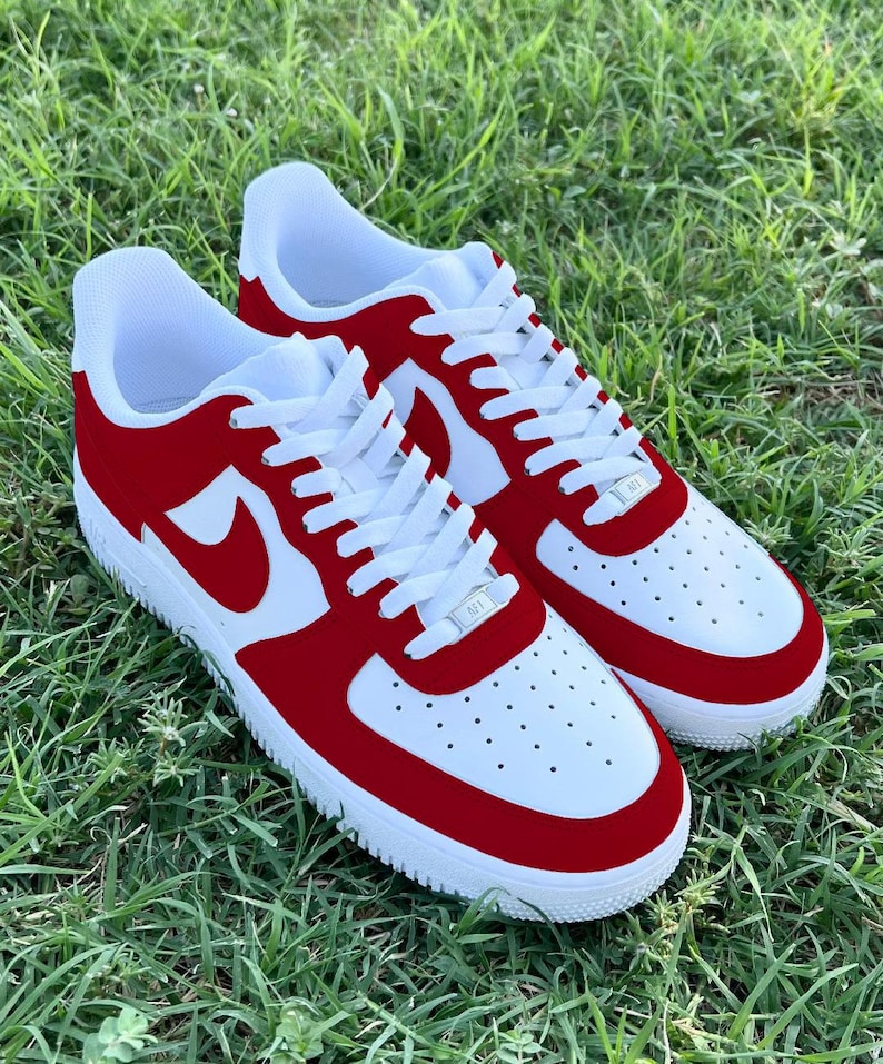 Pu&ograve; includere: Un paio di scarpe da ginnastica bianche e rosse con un logo swoosh bianco. Le scarpe hanno una punta e un tallone in camoscio rosso.