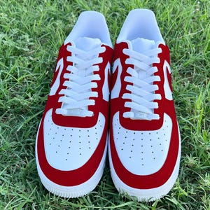 Pu&ograve; includere: Un paio di scarpe da ginnastica bianche e rosse con lacci bianchi. Le scarpe hanno una punta e un tallone in camoscio rosso.