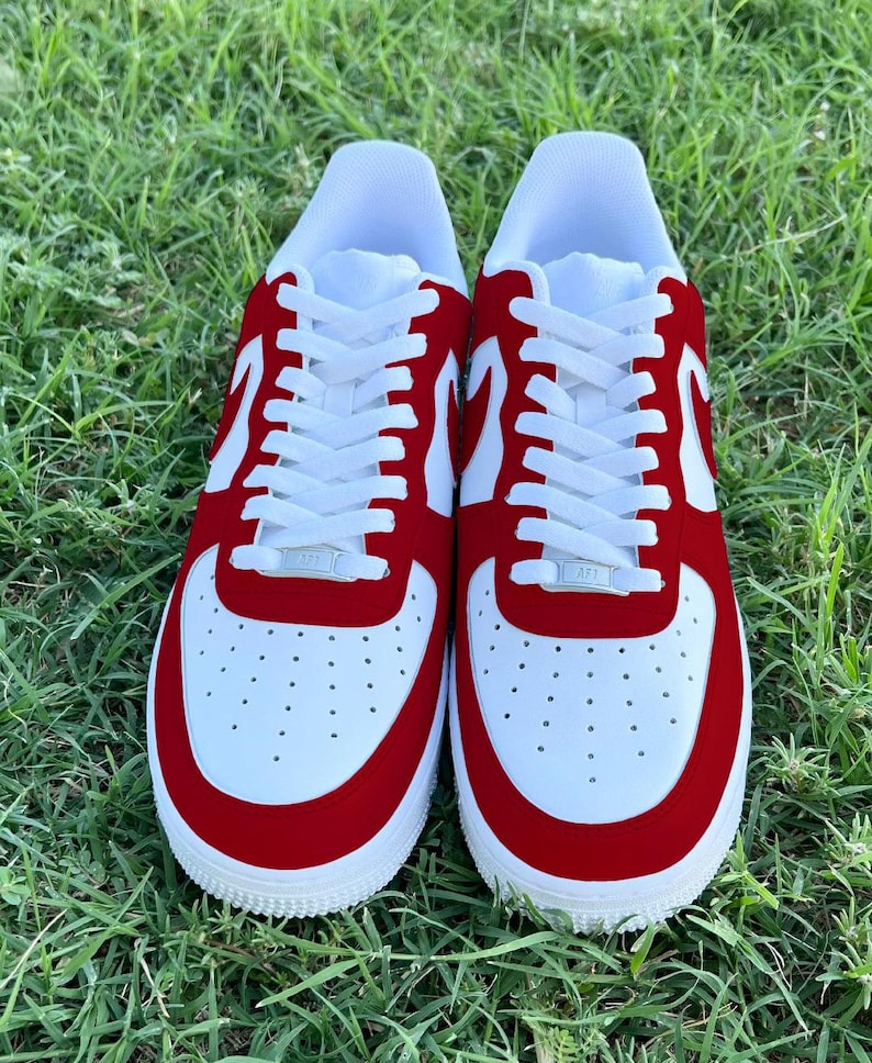 Pu&ograve; includere: Un paio di scarpe da ginnastica bianche e rosse con lacci bianchi. Le scarpe hanno una punta e un tallone in camoscio rosso.