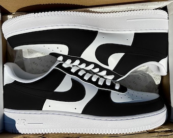 May include: Black and white custom Nike Air Force 1 sneakers with a unique swoosh design. The shoes are in a shoebox.