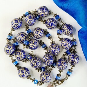 May include: A blue and gold necklace featuring large round beads and a gold chain. The beads have a decorative pattern and are interspersed with small blue crystal beads.