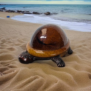 May include: A brown and gold turtle-shaped decorative object with a glossy finish. The turtle is sitting on a sandy beach.