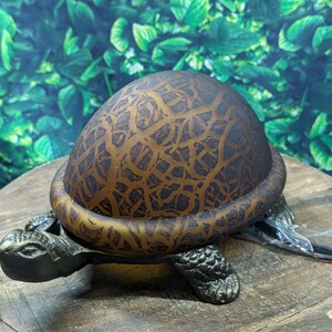 May include: A decorative lamp shaped like a turtle with a brown glass shade featuring a textured pattern. The lamp is on a wooden surface.