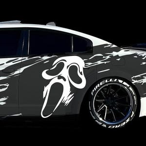 May include: White car with a black and white graphic design featuring a Scream mask. The car has black rims with white lettering on the tires. The design covers the side of the car.