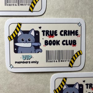 May include: A sticker with the text "TRUE CRIME BOOK CLUB" and a cartoon cat holding a knife. The sticker has a barcode and the words "VIP members only". The design includes yellow and black caution tape and blood splatter.