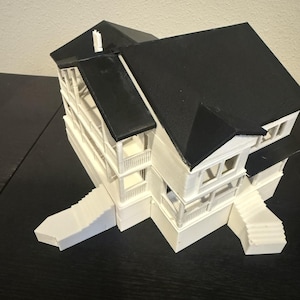 May include: A white and black model house with a two-storey design, featuring a black roof, white balconies, and staircases. The miniature house is a detailed architectural representation.