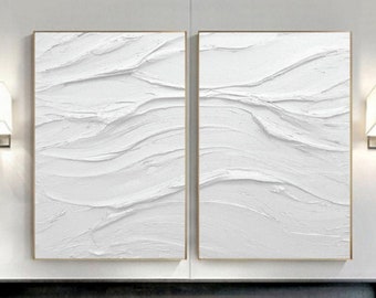 May include: Two white abstract paintings with a textured, wavy design. The paintings are framed in gold and hung on a white wall.