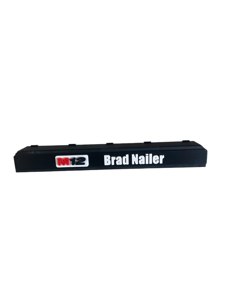 K&ouml;nnte beinhalten: Schwarzer Kunststoffkoffer mit einem wei&szlig;en Etikett mit der Aufschrift "Brad Nailer" und einem roten und wei&szlig;en Etikett mit der Aufschrift "M12".