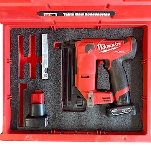 Może przedstawiać: Czerwona gwoździarka do gwoździ brad Milwaukee FUEL 18-gauge z czarną baterią i czarną walizką transportową. Walizka ma napis "Table Saw Accessories" na górze.