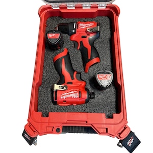 May include: A red and black Milwaukee power tool set in a red carrying case. The set includes a drill, impact driver, and measuring tape. The case is open, revealing the tools nestled in black foam.