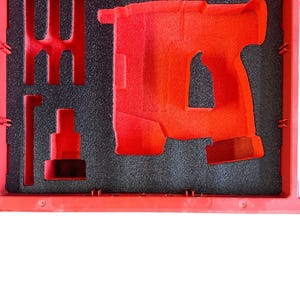 K&ouml;nnte beinhalten: Ein roter, mit Schaumstoff ausgekleideter Koffer mit einer Aussparung f&uuml;r eine Bohrmaschine. Der Koffer hat ein schwarzes Schaumstoff-Innenleben mit einer Aussparung f&uuml;r einen Bohrer.