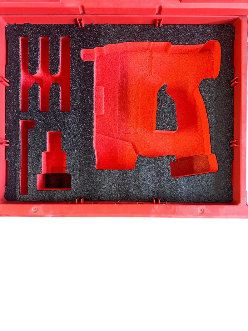 K&ouml;nnte beinhalten: Ein roter, mit Schaumstoff ausgekleideter Koffer mit einer Aussparung f&uuml;r eine Bohrmaschine. Der Koffer hat ein schwarzes Schaumstoff-Innenleben mit einer Aussparung f&uuml;r einen Bohrer.