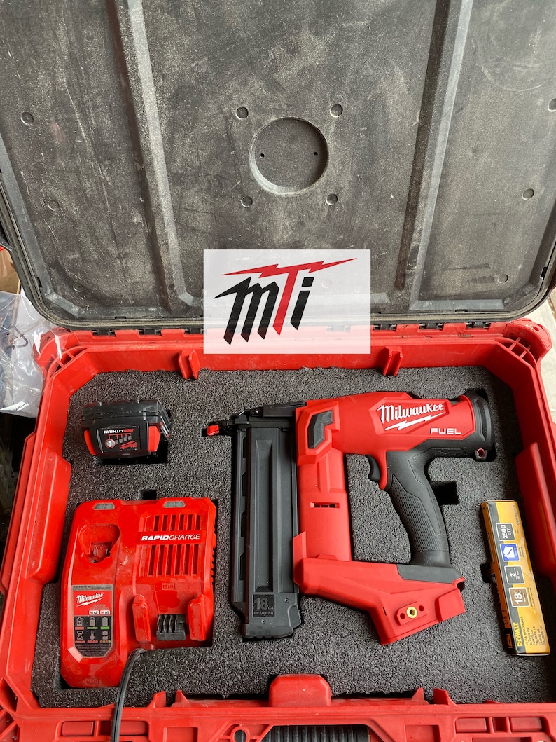 Puede incluir: Una clavadora de brad de calibre 18 Milwaukee FUEL roja con mango negro y un cargador de bater&iacute;a rojo y negro en una caja de herramientas roja. La clavadora tiene un cargador negro y un gatillo negro. El cargador de bater&iacute;a tiene el texto "RAPIDCHARGE" en &eacute;l. La caja de herramientas tiene el texto "Milwaukee" en ella.
