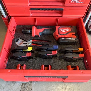 Op de afbeelding: Rode Milwaukee Packout gereedschapskist met een zwarte schuimrubberen inleg. De kist bevat een Milwaukee M18 FUEL 1/2 inch slagmoersleutel, een pijpsnijder en vier zwarte en rode pijpsnijders.