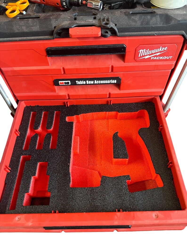 K&ouml;nnte beinhalten: Rote Milwaukee Packout Werkzeugbox mit schwarzem Schaumstoffeinsatz. Der Einsatz hat einen Ausschnitt f&uuml;r ein Elektrowerkzeug. Die Box tr&auml;gt ein Etikett mit der Aufschrift "Table Saw Accessories".
