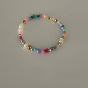 May include: A colorful beaded bracelet with gold beads, white beads, and a variety of colored beads.